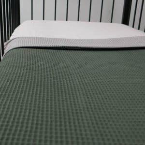 Opgemaakt ledikant met deken van taupe-groene wafelstof.