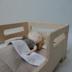 Houten poppenbedje met een slapend popje.