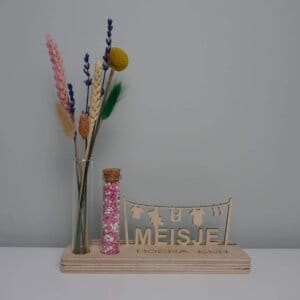 Houten standaard met droogbloemen en blauwe muisjes in glazen buisje met tekst HOERA EEN MEISJE.